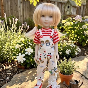 May include: A doll with blonde hair in pigtails wearing a red and white striped shirt under white overalls featuring a repeating print of cartoon characters. The doll wears red and white sneakers with white laces, standing upright with a neutral expression.