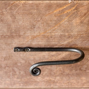 May include: A black metal towel bar with a decorative scroll design. The bar is mounted to a wooden surface with two screws.