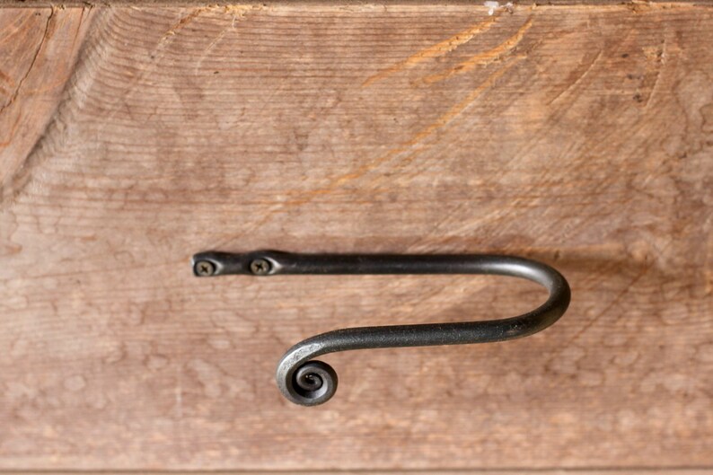 May include: A black metal towel bar with a decorative scroll design. The bar is mounted to a wooden surface with two screws.