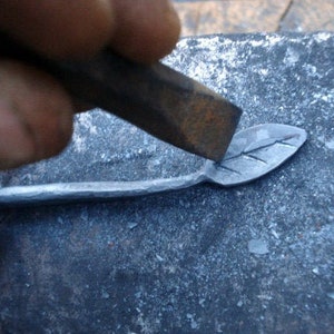 May include: A hand using a metal hammer to shape a leaf design into a piece of metal.