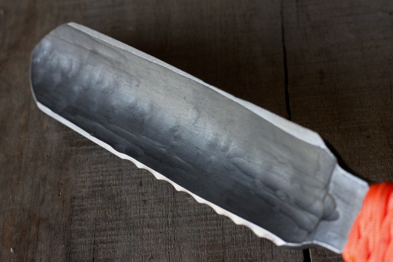 May include: A hand-forged, gray metal shaving scuttle with a textured interior and a scalloped edge. The handle is wrapped in bright orange cord. The scuttle is designed to hold shaving soap and create a rich lather.