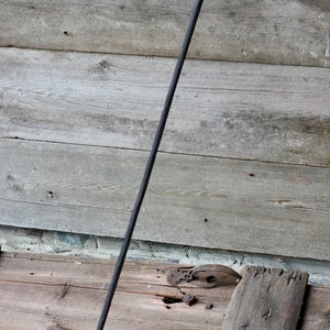 May include: A long, black metal fireplace poker with a forked end. The poker is leaning against a wooden wall.