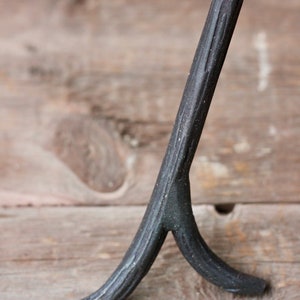 May include: A black metal tripod stand with a textured finish. The stand has three legs that are forked at the bottom.