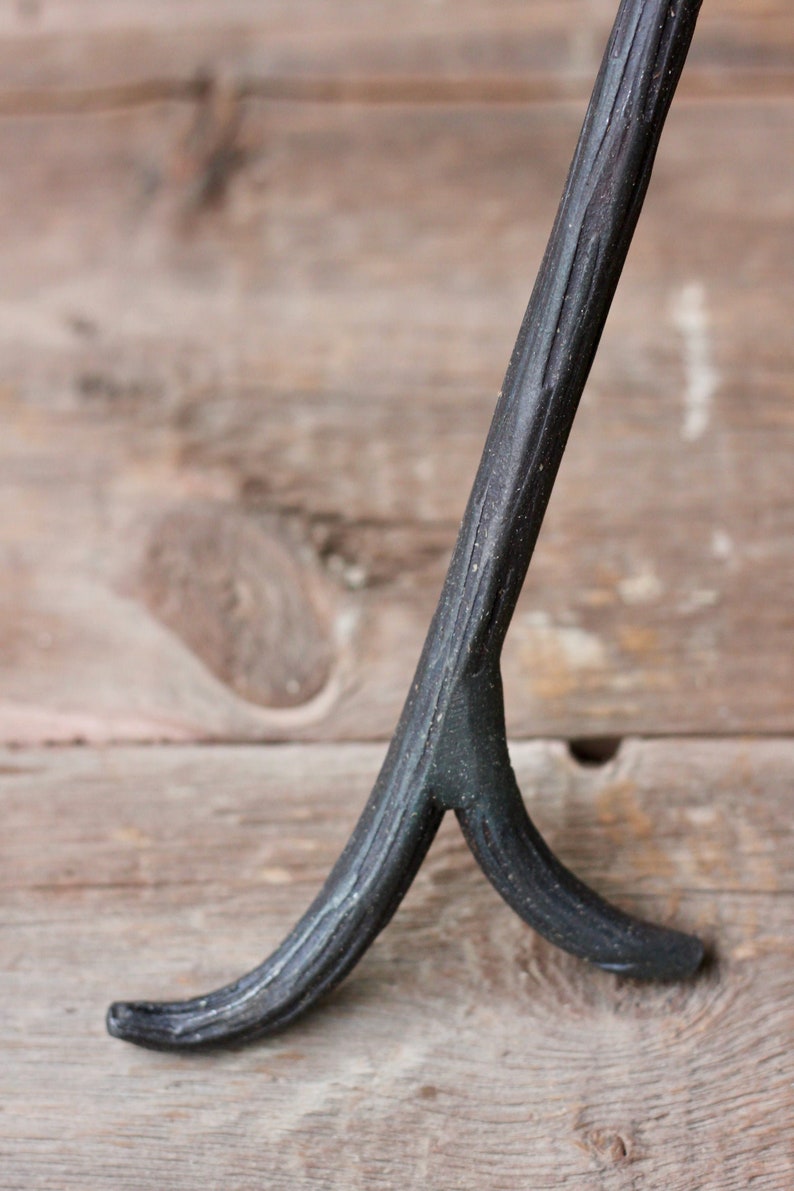 May include: A black metal tripod stand with a textured finish. The stand has three legs that are forked at the bottom.