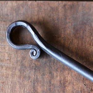 May include: A close-up of a black metal fireplace poker with a decorative, hand-forged handle. The handle is shaped like a loop with a spiral detail.