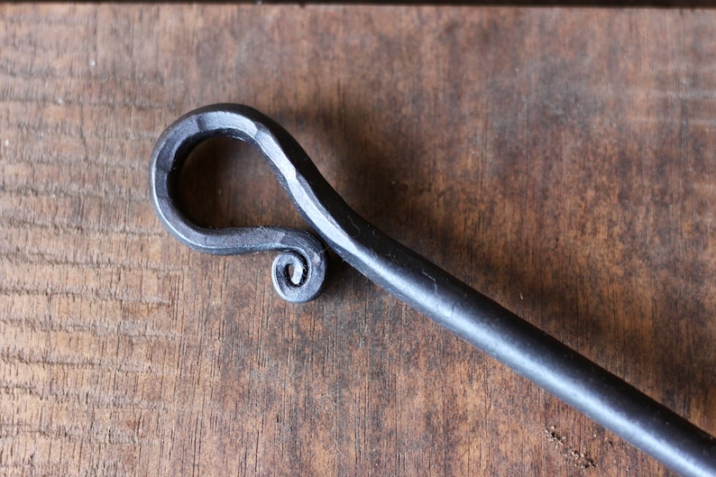 May include: A close-up of a black metal fireplace poker with a decorative, hand-forged handle. The handle is shaped like a loop with a spiral detail.