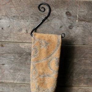 May include: A brown towel with a floral pattern hangs on a black metal hook attached to a wooden wall.