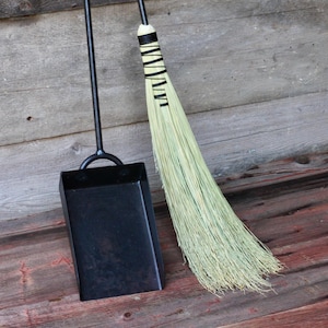 May include: A black metal fireplace shovel and a long-handled broom with a natural straw bristle head and black leather wrappings on the handle.