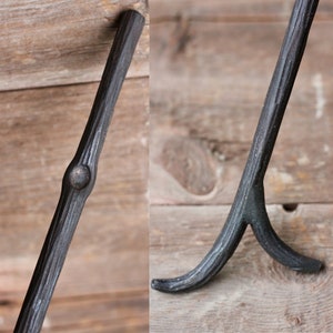 May include: A black metal fireplace tool with a curved handle and a forked end. The tool is made of wrought iron and has a rustic, hand-forged look.