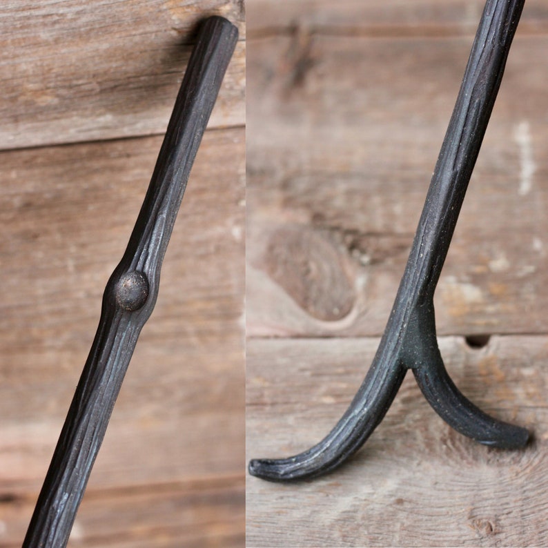 May include: A black metal fireplace tool with a curved handle and a forked end. The tool is made of wrought iron and has a rustic, hand-forged look.
