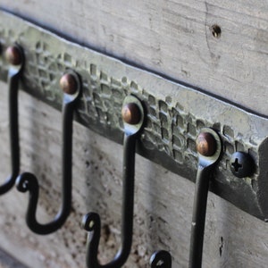 May include: A hammered metal wall hook with three hooks. The hook is black with copper accents. The hook is mounted on a wooden surface.