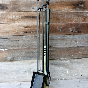 May include: A black metal fireplace tool set with a stand. The set includes a poker, shovel, and brush. The tools are held together by a metal frame.