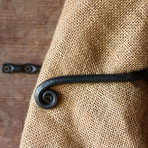 May include: Black metal towel ring with a spiral design. The ring is mounted on a wooden surface and a burlap towel is hanging on it.