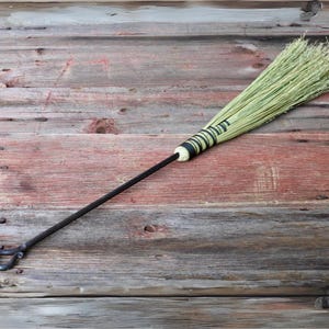 May include: A long-handled broom with a black metal handle and a green and black striped binding. The broom is made of natural materials and has a rustic look.