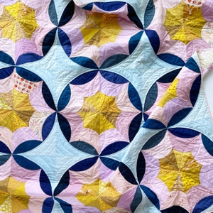 Puede incluir: Una colcha con un patr&oacute;n geom&eacute;trico de c&iacute;rculos superpuestos en tonos de azul, rosa y amarillo. La colcha est&aacute; hecha de retazos de tela y tiene un aspecto cosido a mano.
