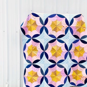 Puede incluir: Una colcha con un patr&oacute;n geom&eacute;trico de c&iacute;rculos rosas, azules y amarillos. La colcha est&aacute; hecha de tela con estampado floral.