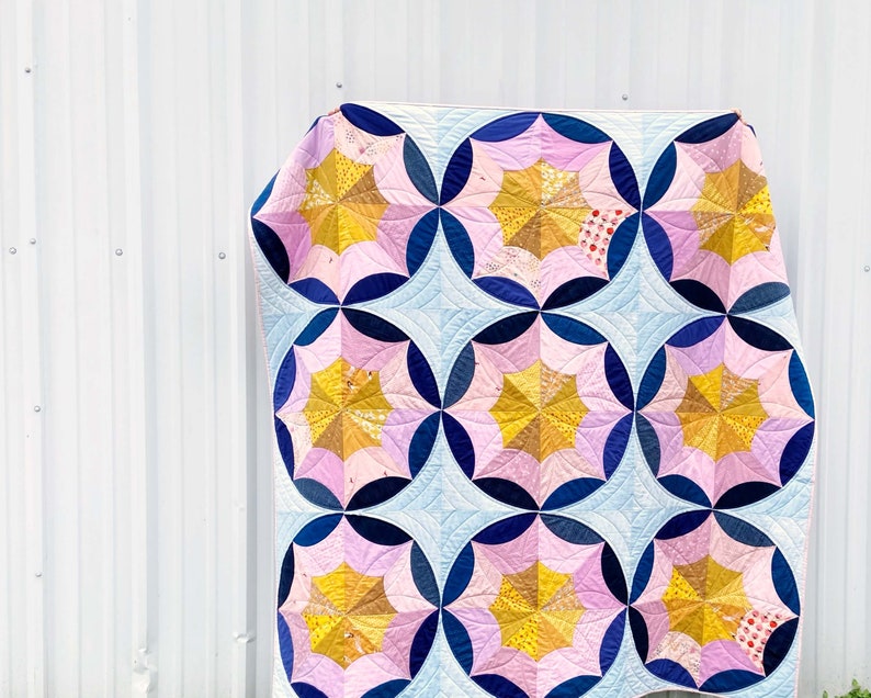Puede incluir: Una colcha con un patr&oacute;n geom&eacute;trico de c&iacute;rculos rosas, azules y amarillos. La colcha est&aacute; hecha de tela con estampado floral.