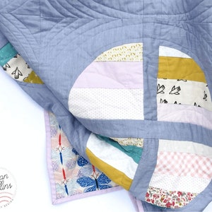 May include: A blue and white patchwork quilt with a variety of patterns, including polka dots, stripes and floral prints. The quilt is folded in half and the edges are visible.