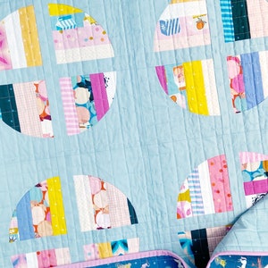 May include: A light blue quilt with a patchwork design featuring colourful circles. The circles are made up of various fabrics with stripes, polka dots, and floral patterns. The quilt is quilted with a diamond pattern.