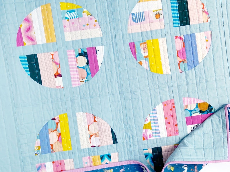 May include: A light blue quilt with a patchwork design featuring colourful circles. The circles are made up of various fabrics with stripes, polka dots, and floral patterns. The quilt is quilted with a diamond pattern.