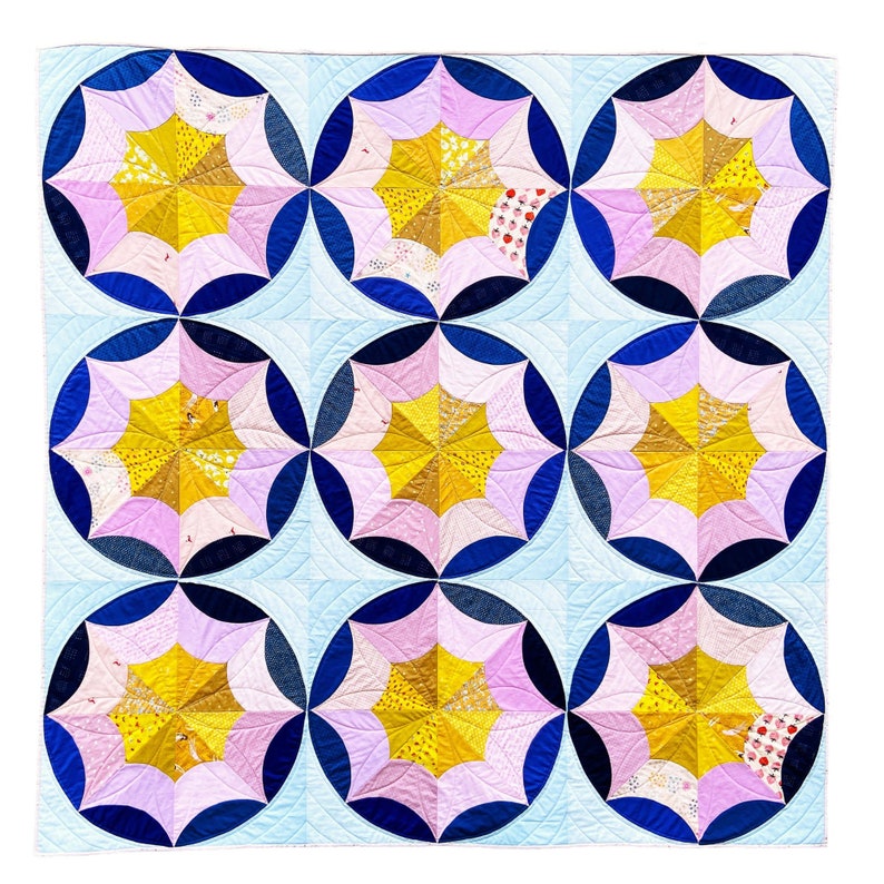 Puede incluir: Una colcha con fondo azul y blanco y nueve parches circulares. Cada parche es un patr&oacute;n de estrella rosa y amarilla.