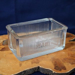 May include: A clear glass salt cellar with a ribbed design and the word "SALT" etched on the front.