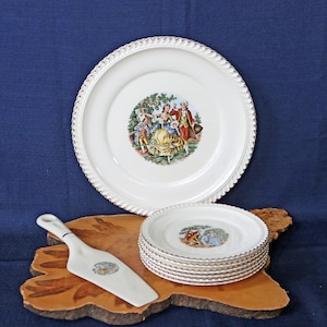 Puede incluir: Un juego de platos de cerámica blanca vintage con borde dorado y un diseño floral con un grupo de personas en un jardín. Los platos están apilados sobre una superficie de madera con un servidor de pastel de cerámica blanca.