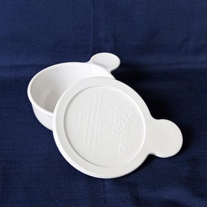May include: White CorningWare dish with a matching lid. The lid and dish have a rounded handle. The lid has the CorningWare logo and text. The dish is on a dark blue background.