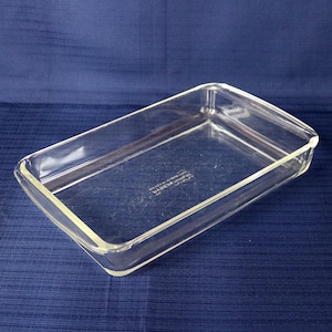 May include: A rectangular clear glass baking dish with rounded corners and a flat bottom. The centre of the dish features embossed text that reads Pyrex Made in USA. The glass is transparent with a smooth finish and a thick, moulded rim.
