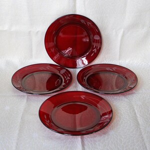 May include: Set of four red glass dinner plates with a white design. The plates are round and have a slightly raised rim.