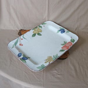 May include: Rectangular serving tray with a light speckled background and a brown trim. The tray is decorated with illustrations of various fruits, including pears, plums, cherries, and peaches, with green leaves. The tray is resting on a wooden surface.