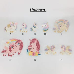 May include: A set of 8 iron-on patches featuring various unicorn designs. The patches are in pink, blue, yellow, and white. The patches are labeled with letters A through H.
