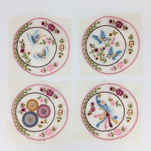May include: Four embroidered fabric patches with pink and green floral designs. The patches feature a blue butterfly, two blue birds, and a blue peacock.