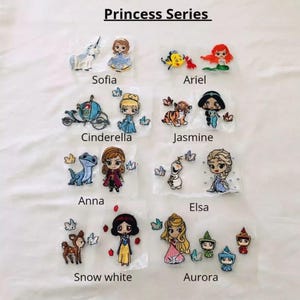 Pode incluir: Um conjunto de 10 patches para passar a ferro com personagens de princesas Disney. Os patches incluem Cinderela, Ariel, Jasmine, Branca de Neve, Aurora, Elsa, Anna, Sofia e dois personagens de Frozen. Os patches estão sobre um fundo branco.