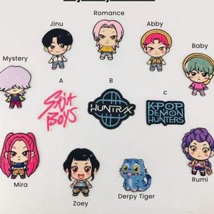 以下が含まれることがあります： 漫画のキャラクターとテキストが刺繍されたパッチのコレクション。パッチには、Jinu、Abby、Baby、Mira、Zoey、Rumiという名前のキャラクターが含まれています。テキストパッチには「Skit Boys」、「Huntrx」、「K-Pop Demon Hunters」と書かれています。