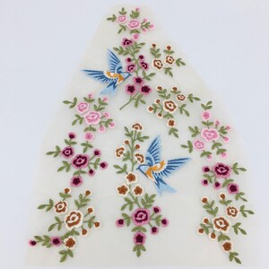 May include: A white sheer fabric with embroidered floral designs and blue birds. The flowers are pink, white, and brown.