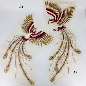 May include: Two embroidered phoenix patches. The birds feature white bodies, red and gold wings, and long, flowing tail feathers. The patches are on a sheer, off-white fabric.