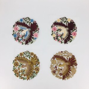 May include: Four embroidered patches featuring a bird with outstretched wings surrounded by flowers. The patches are circular and have a white background. The birds are in different colors: red, blue, gold, and brown.