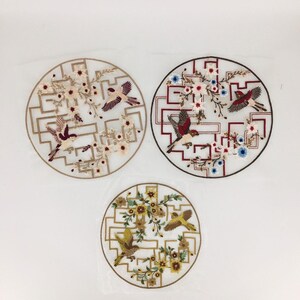 May include: Three embroidered circular patches featuring birds and floral designs. The patches have a geometric border and are in shades of beige, red, brown, yellow, and blue. The birds are in flight, and the flowers are in bloom.