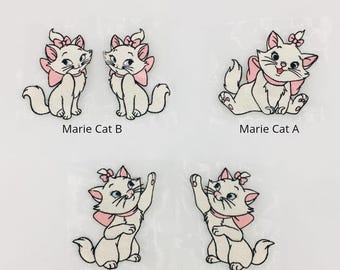 Puede incluir: Cuatro parches bordados para planchar de Marie la gata de Los Aristogatos de Disney. Los parches son blancos con detalles rosas y muestran a Marie en diferentes poses. Los parches están etiquetados como "Marie Cat A", "Marie Cat B" y "Marie Cat C".