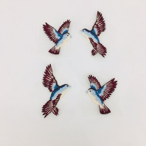 May include: Four embroidered iron-on patches of blue birds with maroon wings. The birds are in flight with their wings spread.