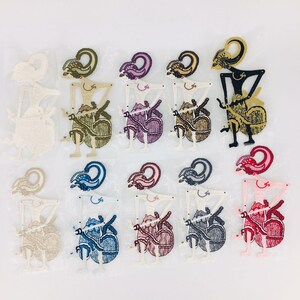 Op de afbeelding: Een set van 12 kleurrijke schaduwpoppen, die elk een figuur met een uniek ontwerp voorstellen. De poppen zijn gemaakt van papier en hebben ingewikkelde details. De poppen zijn in een rij op een witte achtergrond gerangschikt.