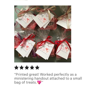 Puede incluir: Un conjunto de peque&ntilde;as bolsas de celof&aacute;n transparentes llenas de caramelos y atadas con una cinta roja. Cada bolsa tiene una peque&ntilde;a etiqueta blanca adjunta con el texto "HE Loves You and We Do Too!" impreso en rosa y negro.