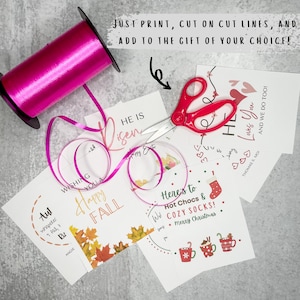 Puede incluir: Cuatro etiquetas de regalo imprimibles con diferentes dise&ntilde;os y textos. Las etiquetas est&aacute;n sobre una superficie gris con una cinta rosa y unas tijeras. El texto en las etiquetas incluye "Wishing you a Happy Fall", "He is Risen", "Here's to Hot Chocs & Cozy Socks! Merry Christmas", y "My Loves You & We Do Too!"