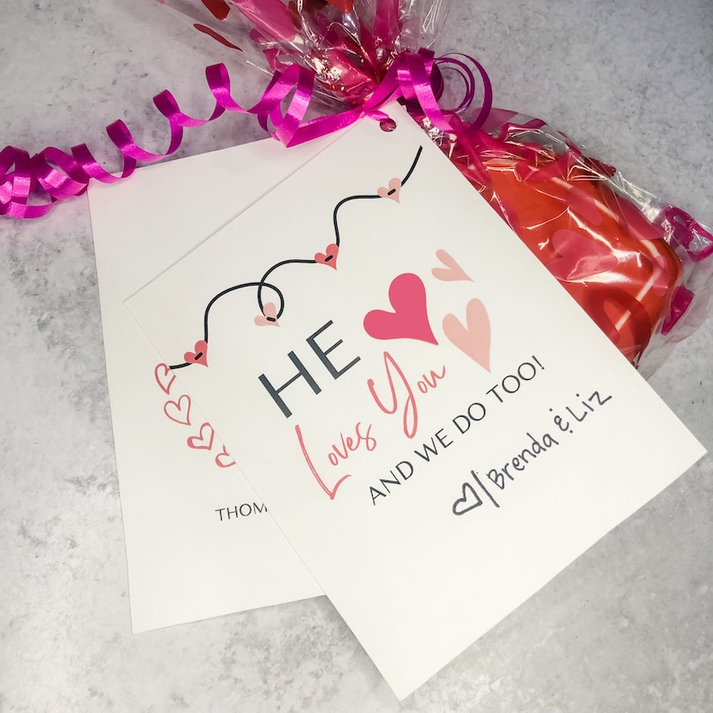 Puede incluir: Una tarjeta blanca con corazones rosas y texto negro que dice "HE Loves You AND WE DO TOO!  Brenda & Liz".