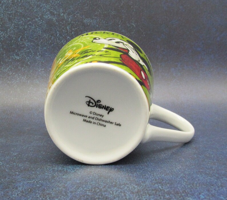 Puede incluir: Taza de cer&aacute;mica blanca con un dise&ntilde;o verde, rojo y amarillo con Mickey Mouse y el texto "Mickey Mouse Clubhouse". La parte inferior de la taza tiene el texto "Disney", "Microwave and Dishwasher Safe", y "Made in China".