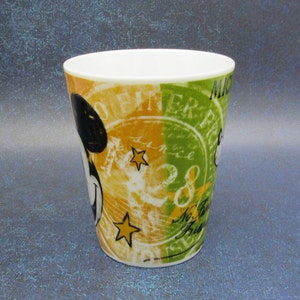 Puede incluir: Una taza de cer&aacute;mica blanca con un dise&ntilde;o colorido que presenta a Mickey Mouse, estrellas y el texto "Mickey Mouse" y "Offiner Era".