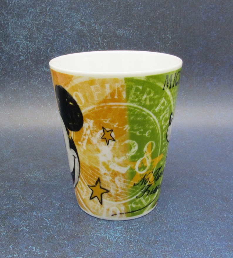 Puede incluir: Una taza de cer&aacute;mica blanca con un dise&ntilde;o colorido que presenta a Mickey Mouse, estrellas y el texto "Mickey Mouse" y "Offiner Era".