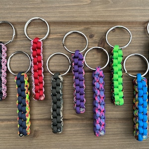 May include: Nine colorful paracord keychains with silver key rings. The keychains are made with different colored paracord and have a variety of patterns.