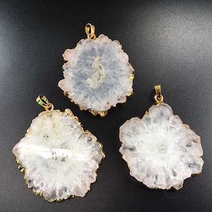 May include: Three white quartz crystal pendants with gold-toned edges. The crystals are in the shape of a flower with a clear center and white edges.